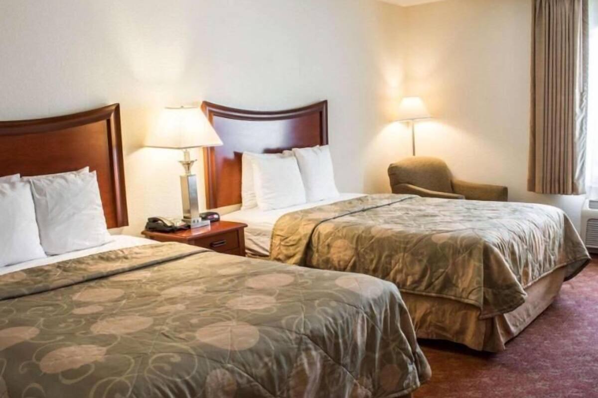 A hotel room with two beds, bedside lamps, a chair, and a window with curtains.