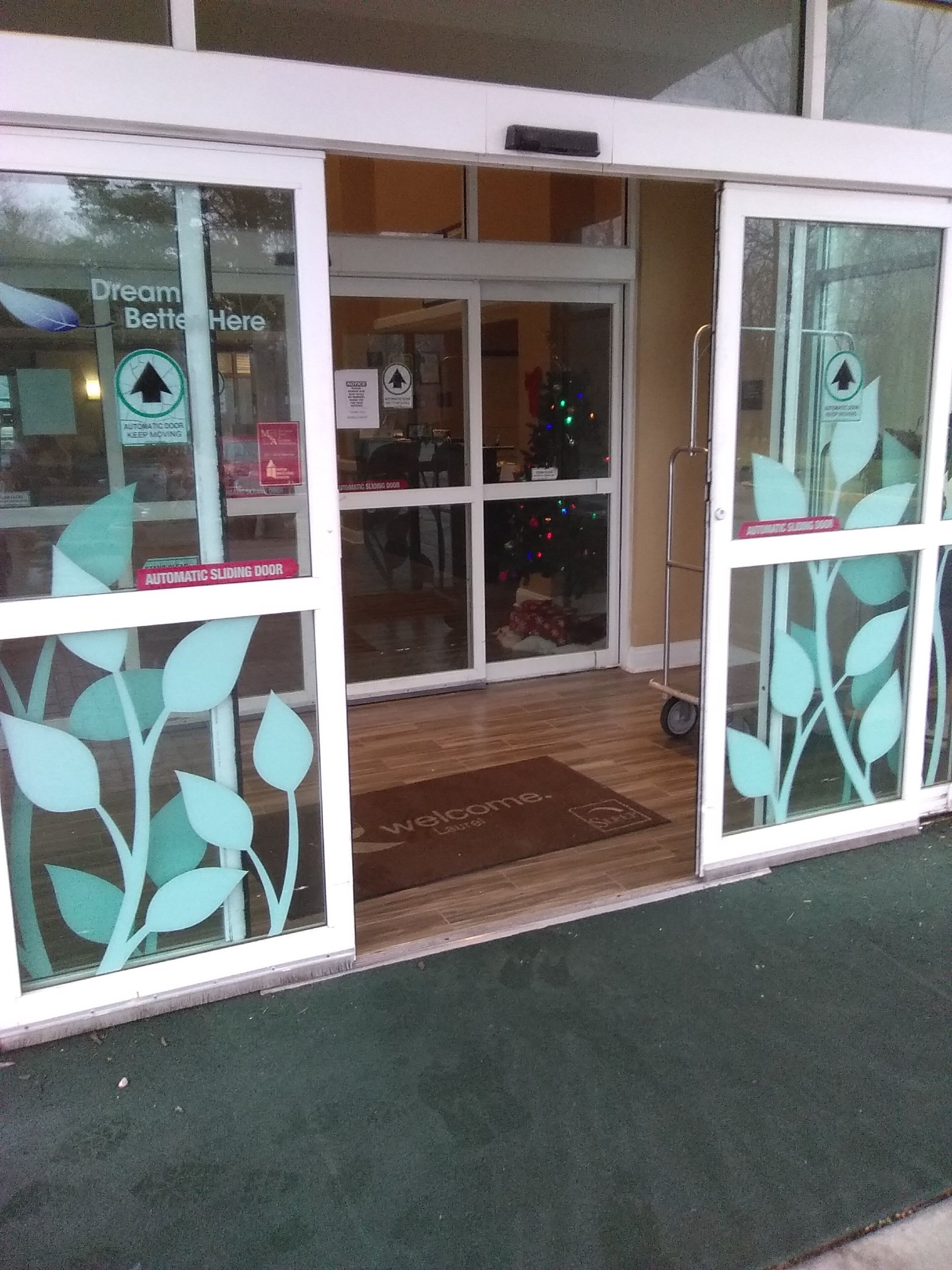 A building entrance with automatic sliding doors, a Christmas tree, and a welcome mat.