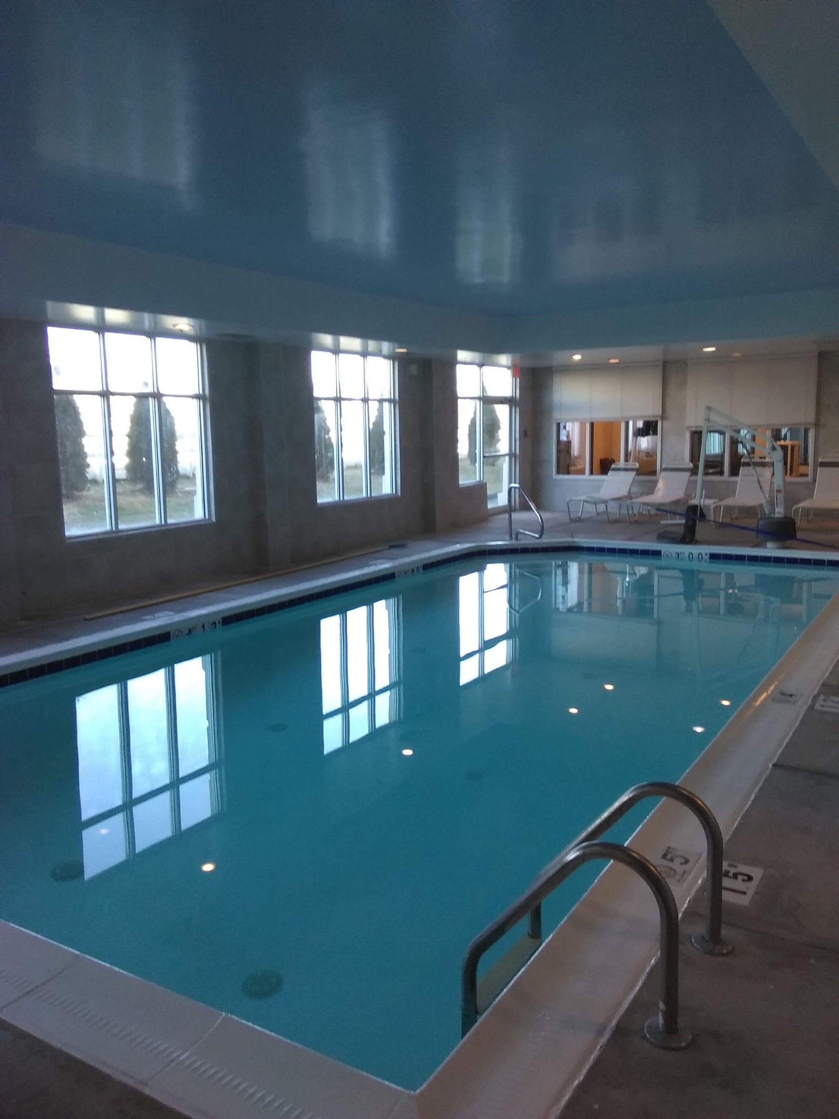Una piscina interior con ventanas transparentes, una silla de salvavidas y un vestuario al fondo.