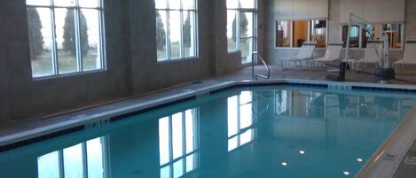 Una piscina interior con ventanas transparentes, una silla de salvavidas y un vestuario al fondo.