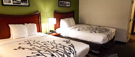 Habitación de hotel con dos camas, una mesita de noche, una silla y una pared con cuadros enmarcados.
