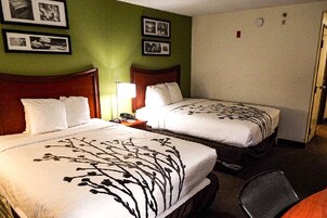 Habitación de hotel con dos camas, una mesita de noche, una silla y una pared con cuadros enmarcados.