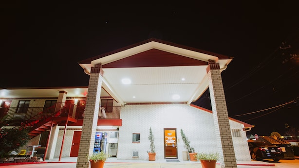 A hotel with a red and white facade, a covered entrance, and potted plants at the entrance. - Palace Inn Wayside (Houston)