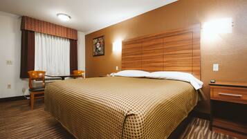 Habitación de hotel con una cama grande, cabecera de madera, escritorio con silla, mesita de noche y ventana con cortinas.