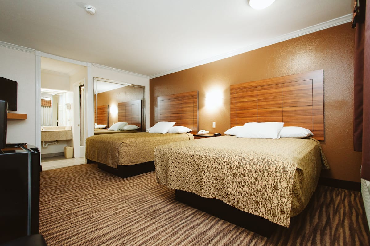 A hotel room with two beds, a bathroom, and a TV.