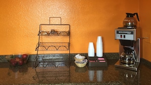 A coffee station with a coffee maker, cups, and a fruit bowl. - Palace Inn Wayside (Houston)