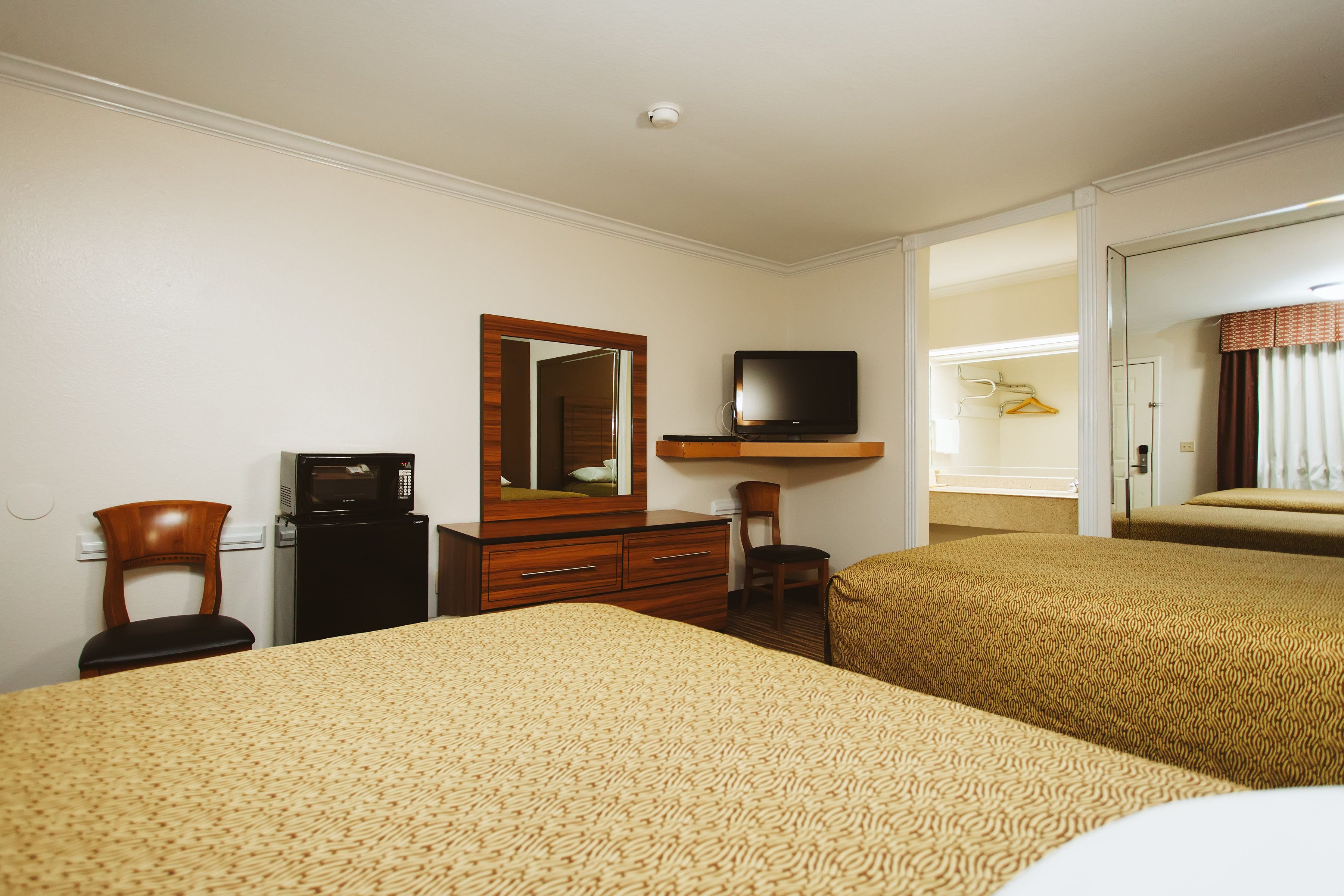 A hotel room with two beds, a desk with a computer, a TV, and a mirror.
