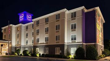A multi-story hotel with a prominent neon sign, a parking lot, and a landscaped entrance area.