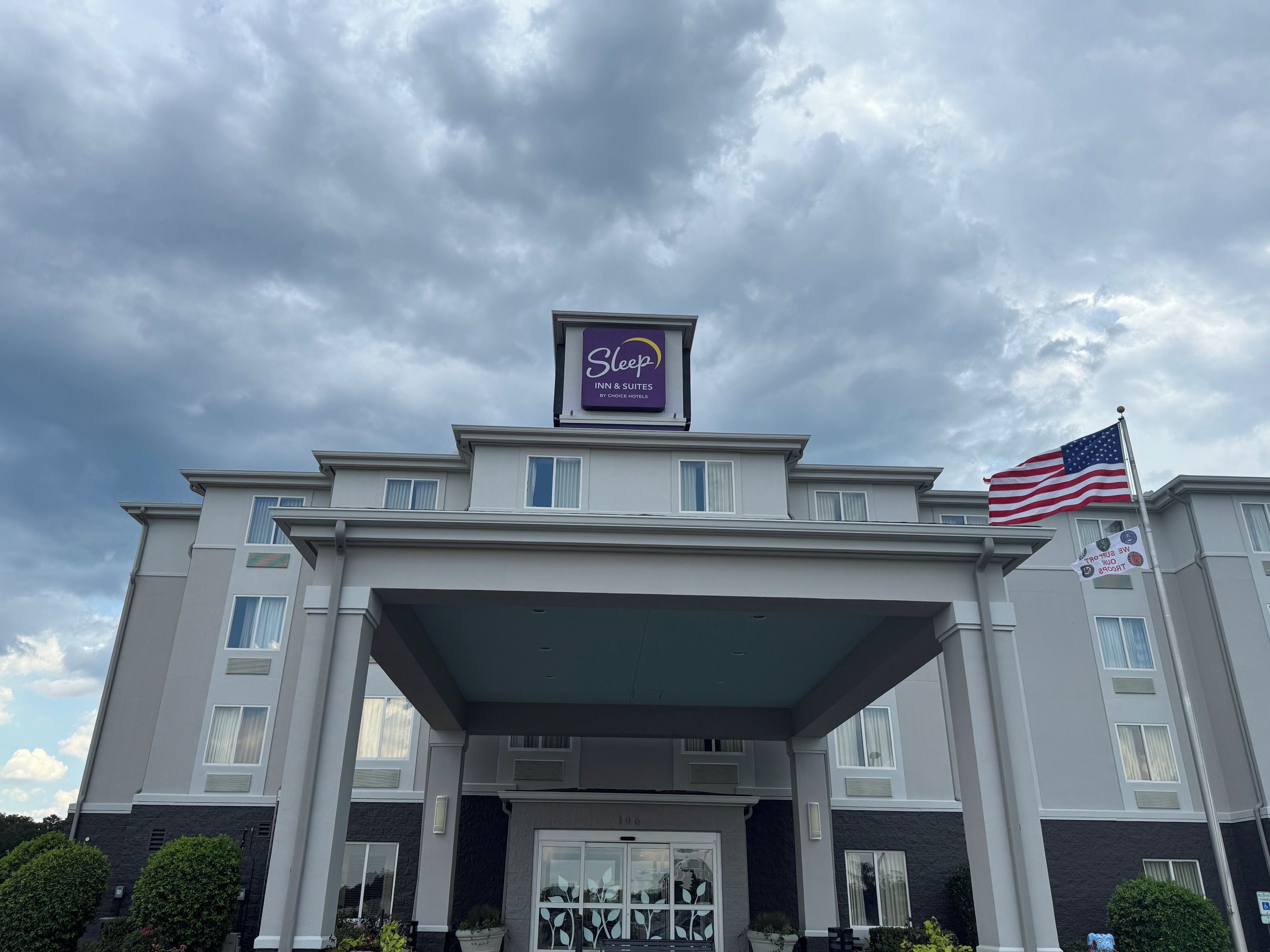 A hotel with a covered entrance, an American flag, and a sign indicating it is a Sleep Inn & Suites.