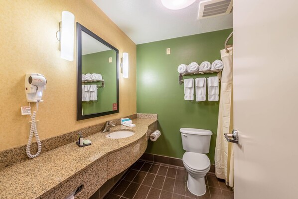 A bathroom with a granite countertop, a sink, a toilet, a hairdryer, and a towel rack with towels.
