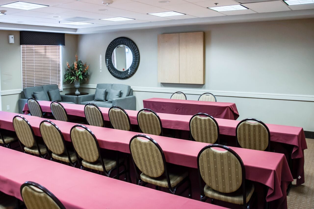 Une salle de conférence avec des rangées de tables et de chaises, un canapé et un miroir au mur.