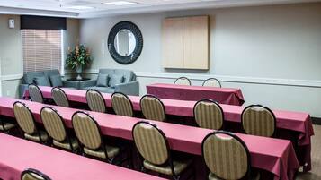 Une salle de conférence avec des rangées de tables et de chaises, un canapé et un miroir au mur.