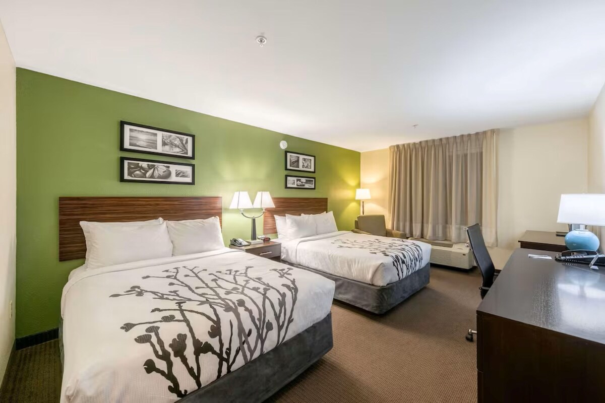 A hotel room with two beds, a desk, and a chair.