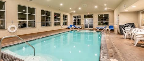 An indoor swimming pool with clear water, a lifeguard chair, and lounge chairs.