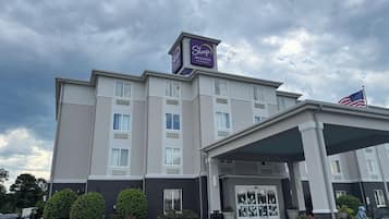 Un hotel Sleep Inn & Suites con entrada cubierta, estacionamiento y una bandera.