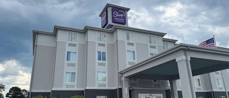 A Sleep Inn & Suites hotel with a covered entrance, a parking lot, and a flag.