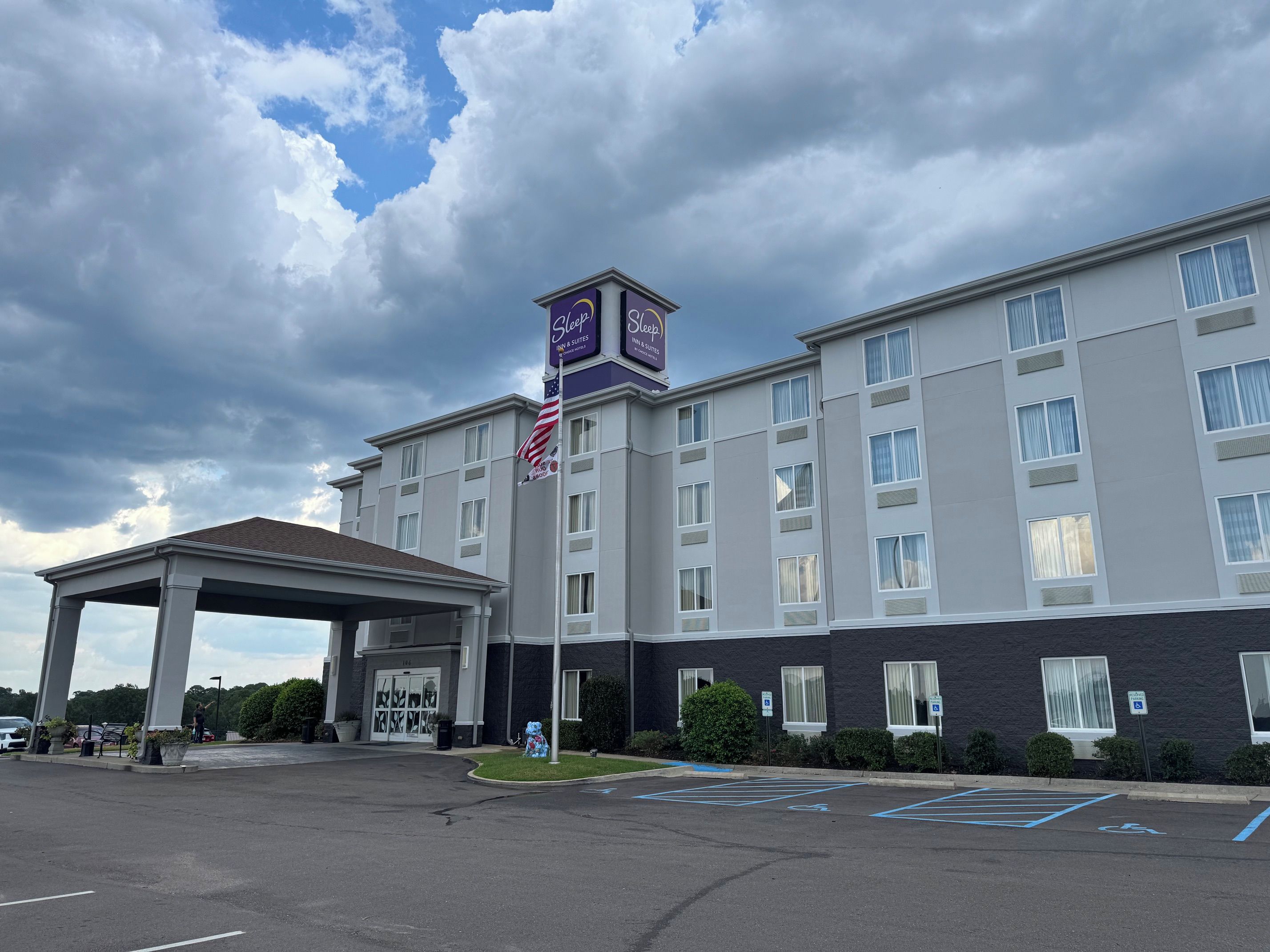 A multi-story hotel with a covered entrance, a flag, and a sign indicating it is a Sleep Inn & Suites.