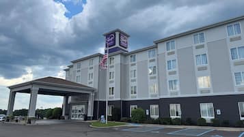 A multi-story hotel with a covered entrance, a flag, and a sign indicating it is a Sleep Inn & Suites.