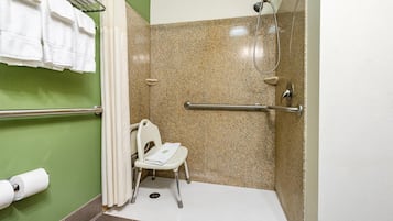 Une douche adaptée aux personnes en fauteuil roulant, équipée d’une barre d’appui, de toilettes avec un siège adapté aux fauteuils roulants et d’un porte-serviettes avec des serviettes.