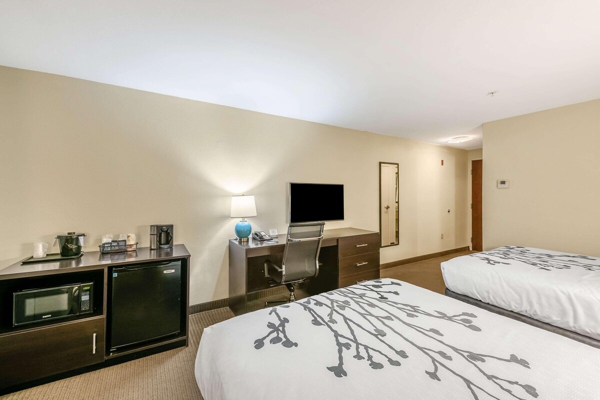 Una habitación de hotel con cama, escritorio con computadora, televisor, minibar y cafetera.