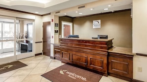 Un área de recepción con mostrador de madera, un cartel de Sleep Inn & Suites y una alfombra de bienvenida.