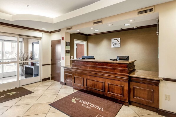 Un área de recepción con mostrador de madera, un cartel de Sleep Inn & Suites y una alfombra de bienvenida.
