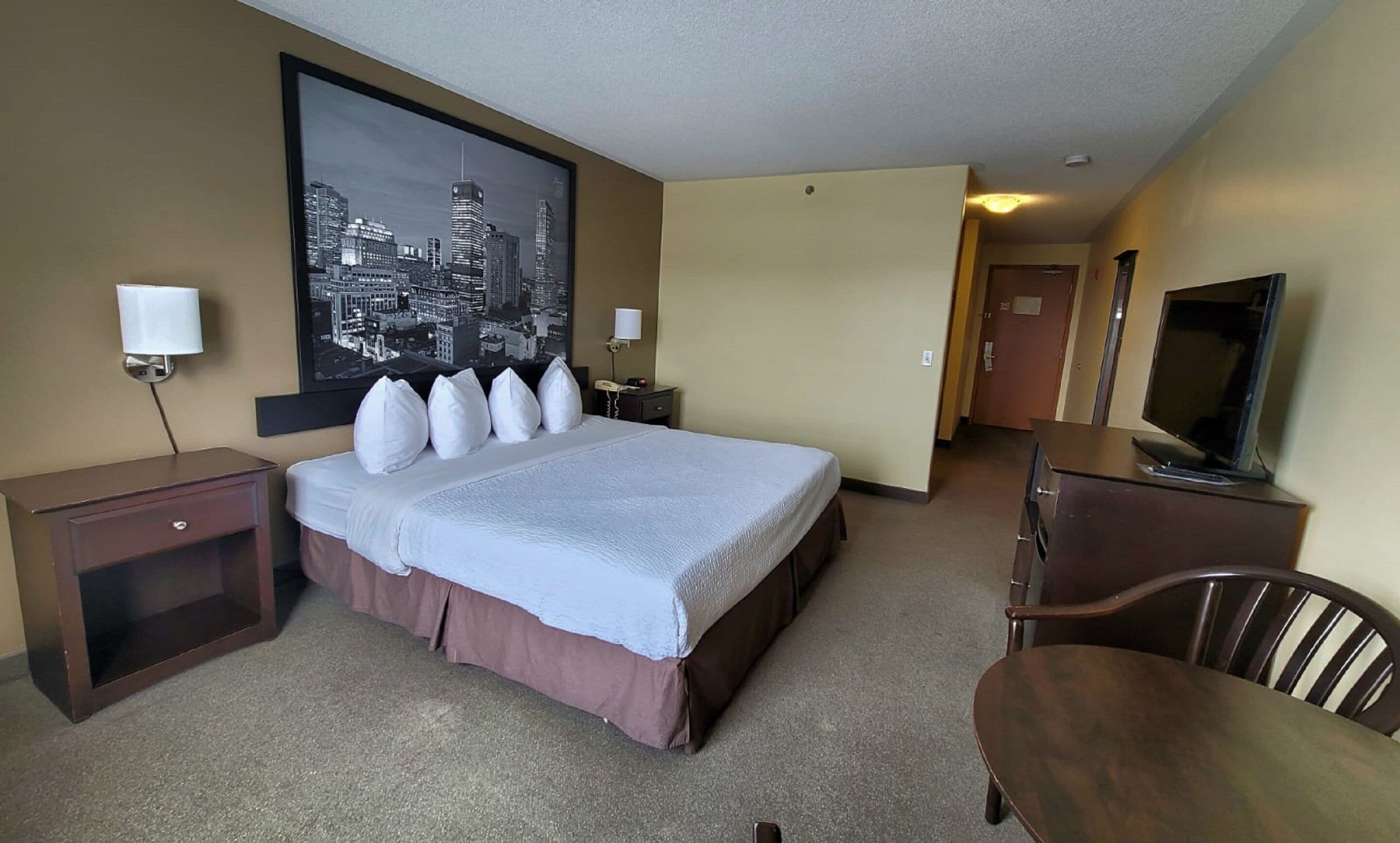 Een hotelkamer met een groot bed, nachtlampjes, een bureau, een stoel, een televisie en uitzicht op de stad.