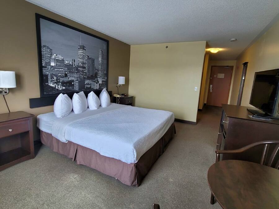 A hotel room with a large bed, bedside lamps, a desk, a chair, a television, and a cityscape view.