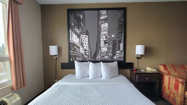 A hotel room with a large bed, two bedside lamps, a nightstand, and a cityscape painting on the wall. - Super 8 by Wyndham Barrie South (Barrie)