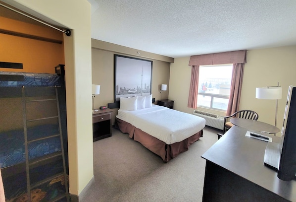 Habitación de hotel con cama, escritorio, silla y un ventanal con cortinas.
