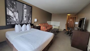 A hotel room with a large bed, a sofa, a desk, a television, and a large cityscape painting on the wall.