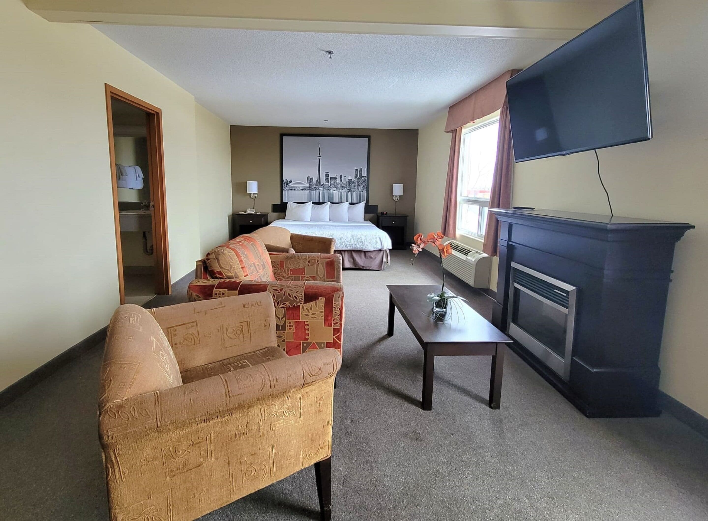 Una habitación de hotel con cama, sofá, una mesita, chimenea y televisor montado en la pared.