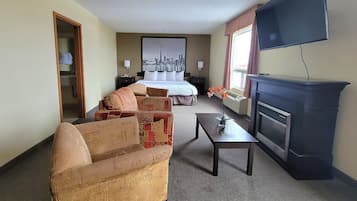 Une chambre d’hôtel comprenant un lit, un canapé, une petite table, une cheminée et un téléviseur fixé au mur.