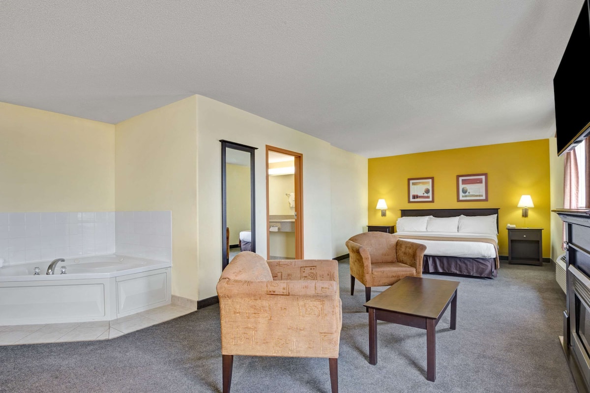 Une chambre d’hôtel avec une baignoire, deux fauteuils, un lit avec une tête de lit, une table de chevet et une lampe.