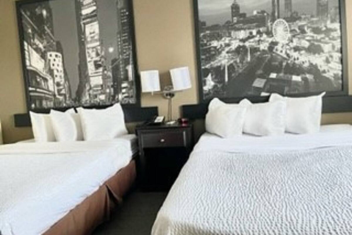Une chambre d’hôtel avec deux lits, une table de chevet et un grand tableau représentant un paysage urbain accroché au mur.