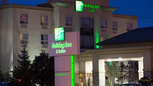 Edificio de Holiday Inn & Suites con señalización iluminada, fachada de piedra y un estacionamiento con vehículos.
