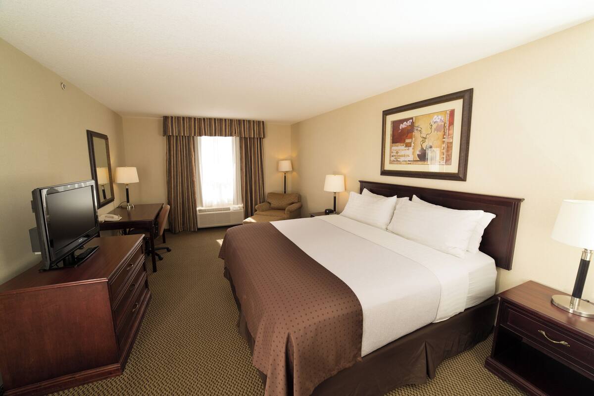 Une chambre d’hôtel avec un grand lit, un bureau doté d’un téléviseur à écran plat, une chaise, une table de chevet et une lampe.