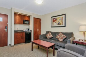 A compact living space with a kitchenette, a sofa with patterned cushions, a small table, and a lamp. - Holiday Inn Hotel & Suites Lloydminster by IHG (Lloydminster)