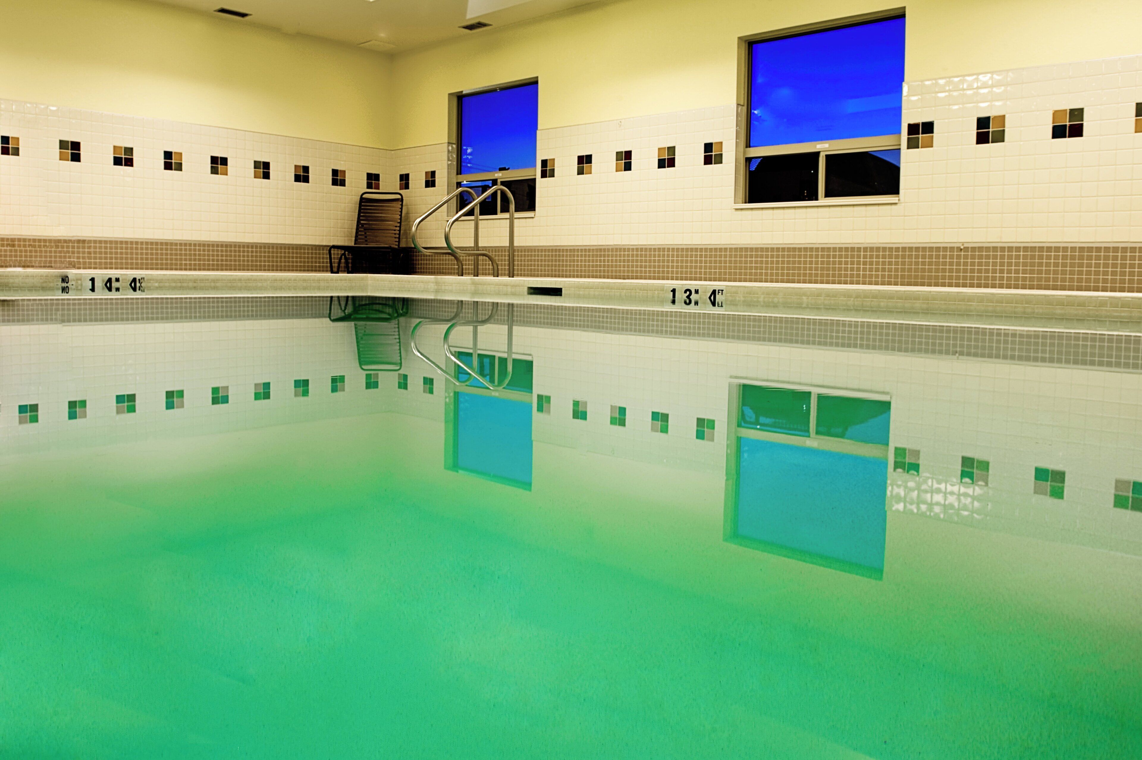 An indoor swimming pool with clear water, tiled walls, and a visible depth marker.