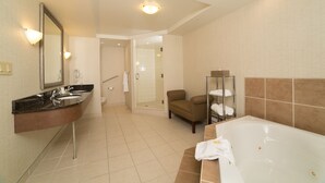 A modern bathroom with a large bathtub, a separate shower area, and a seating area with towels. - Holiday Inn Hotel & Suites Lloydminster by IHG (Lloydminster)