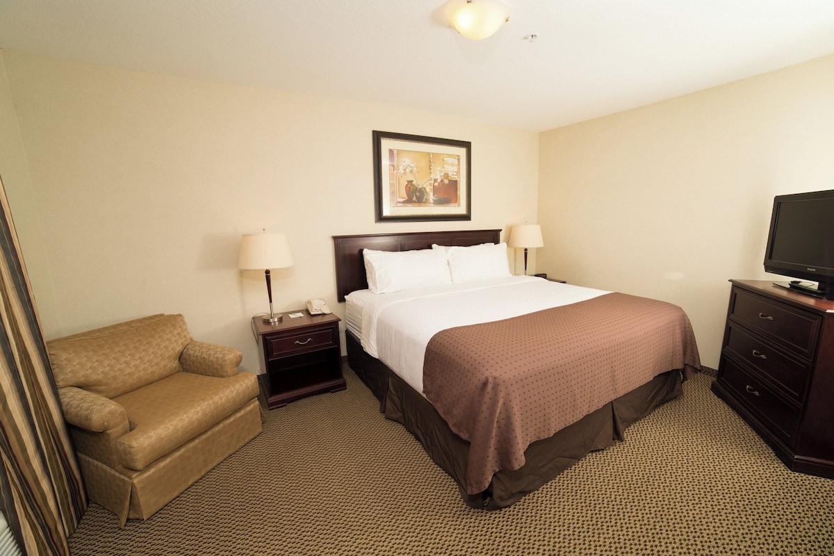 A hotel room with a bed, a chair, a TV, and a nightstand with a lamp.