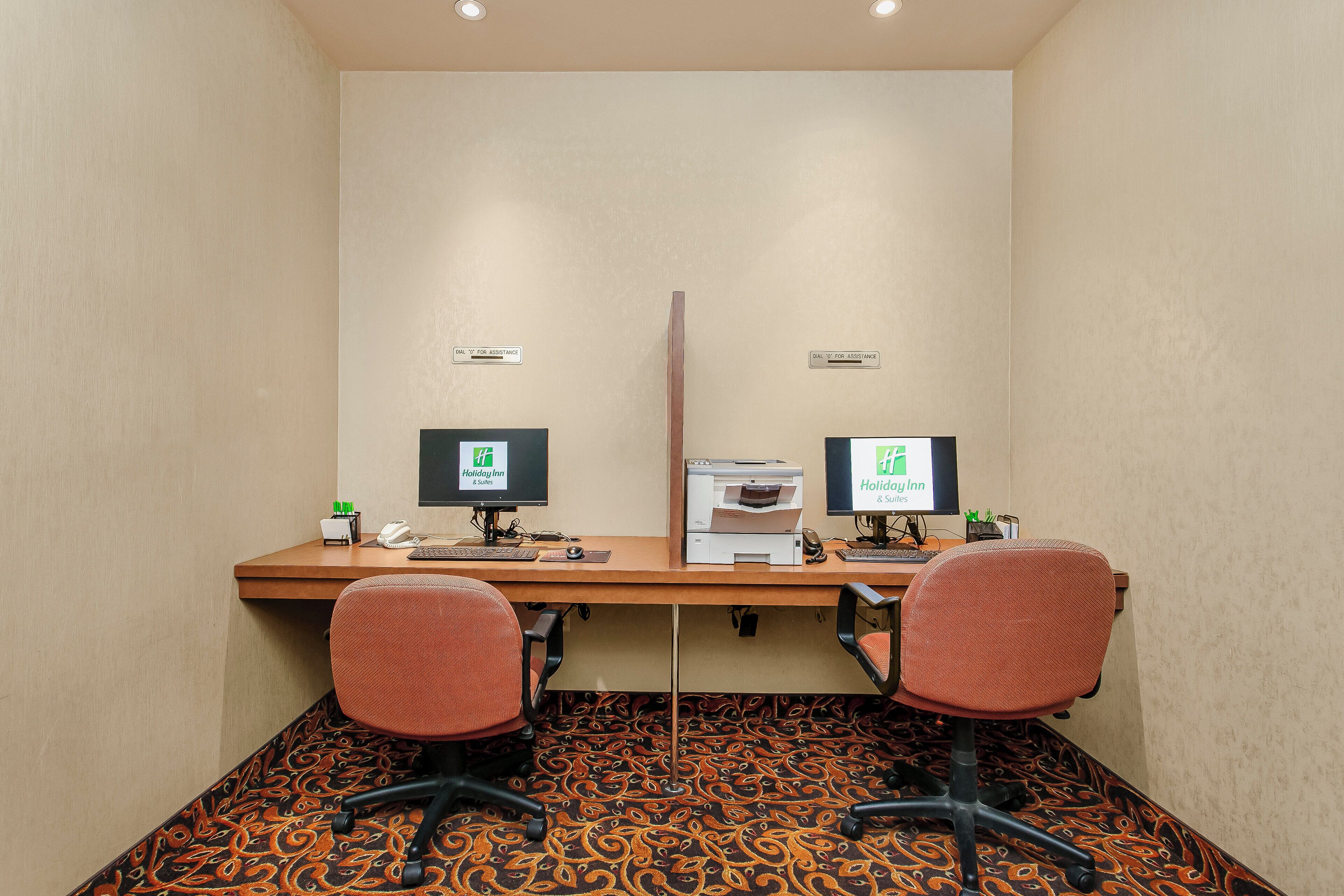 Habitación de hotel con escritorio, dos sillas, una impresora y dos monitores.