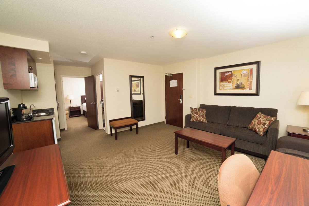 Une chambre d’hôtel comprenant un coin salon, une kitchenette et une porte donnant sur une chambre à coucher.