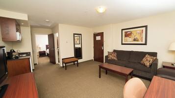 A hotel room with a living area, kitchenette, and a door leading to a bedroom.