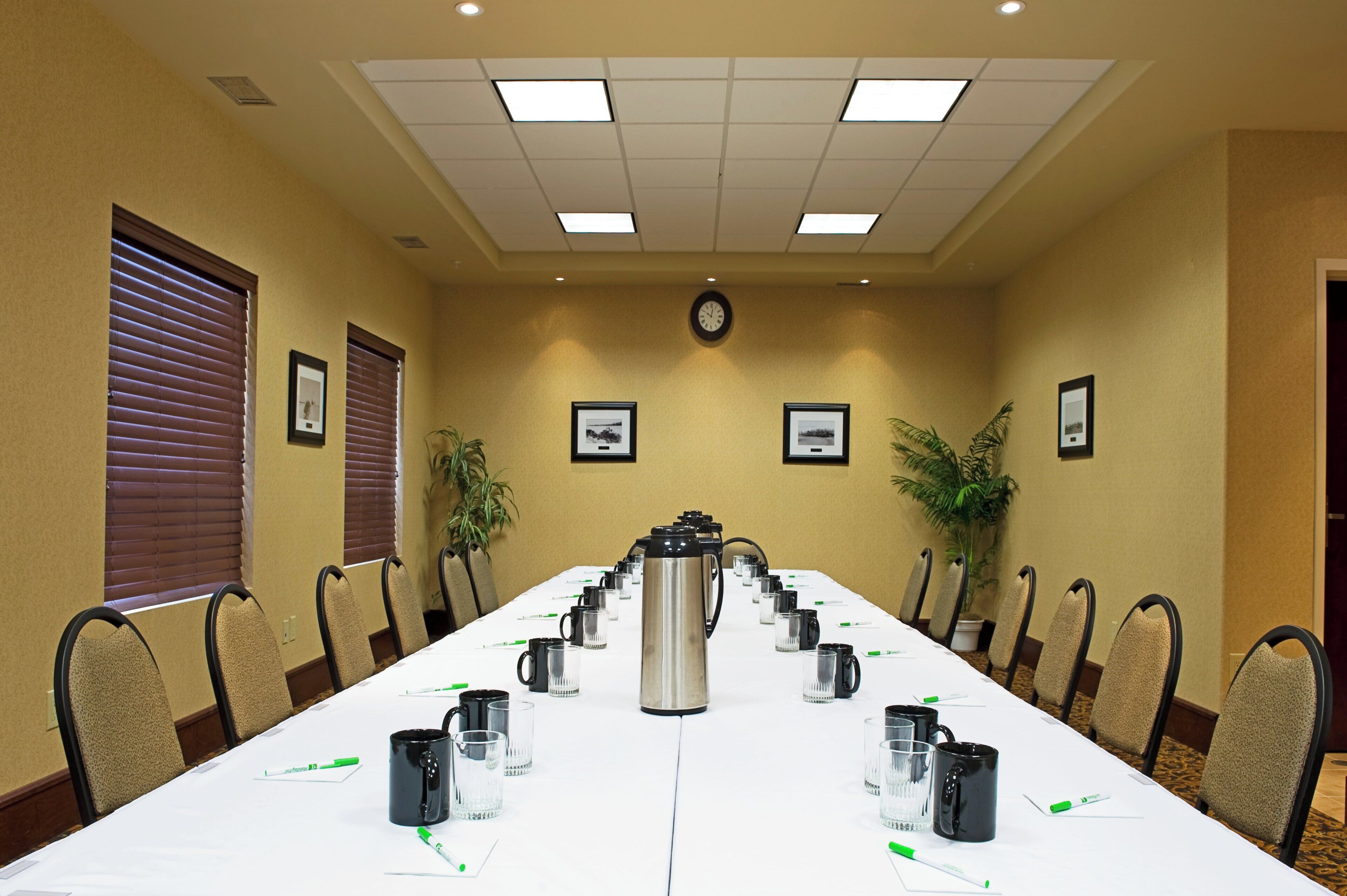 Uma sala de conferência com uma mesa comprida, cadeiras, uma cafeteira e quadros nas paredes.