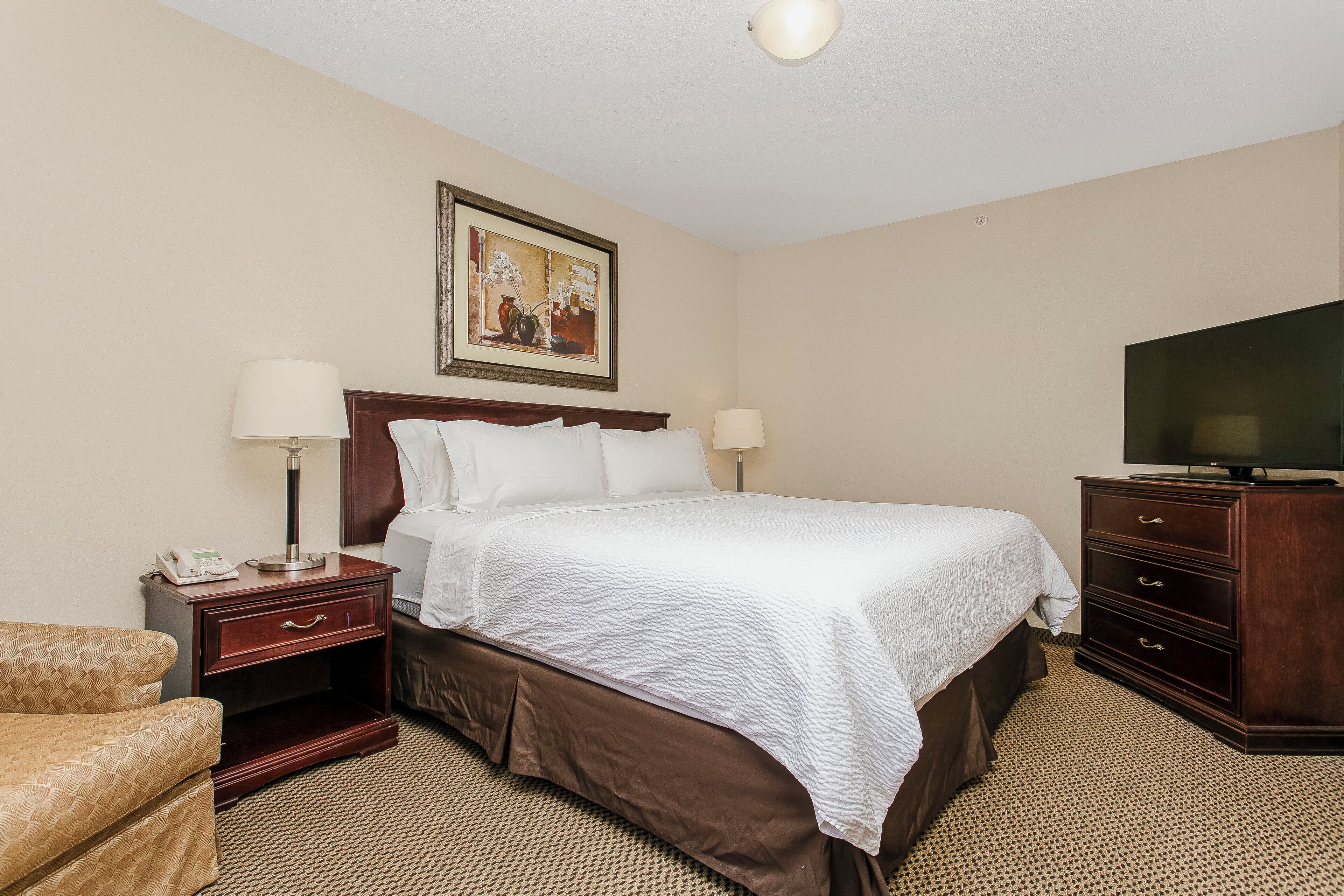 A hotel room with a large bed, two bedside tables, a TV, and a painting on the wall.