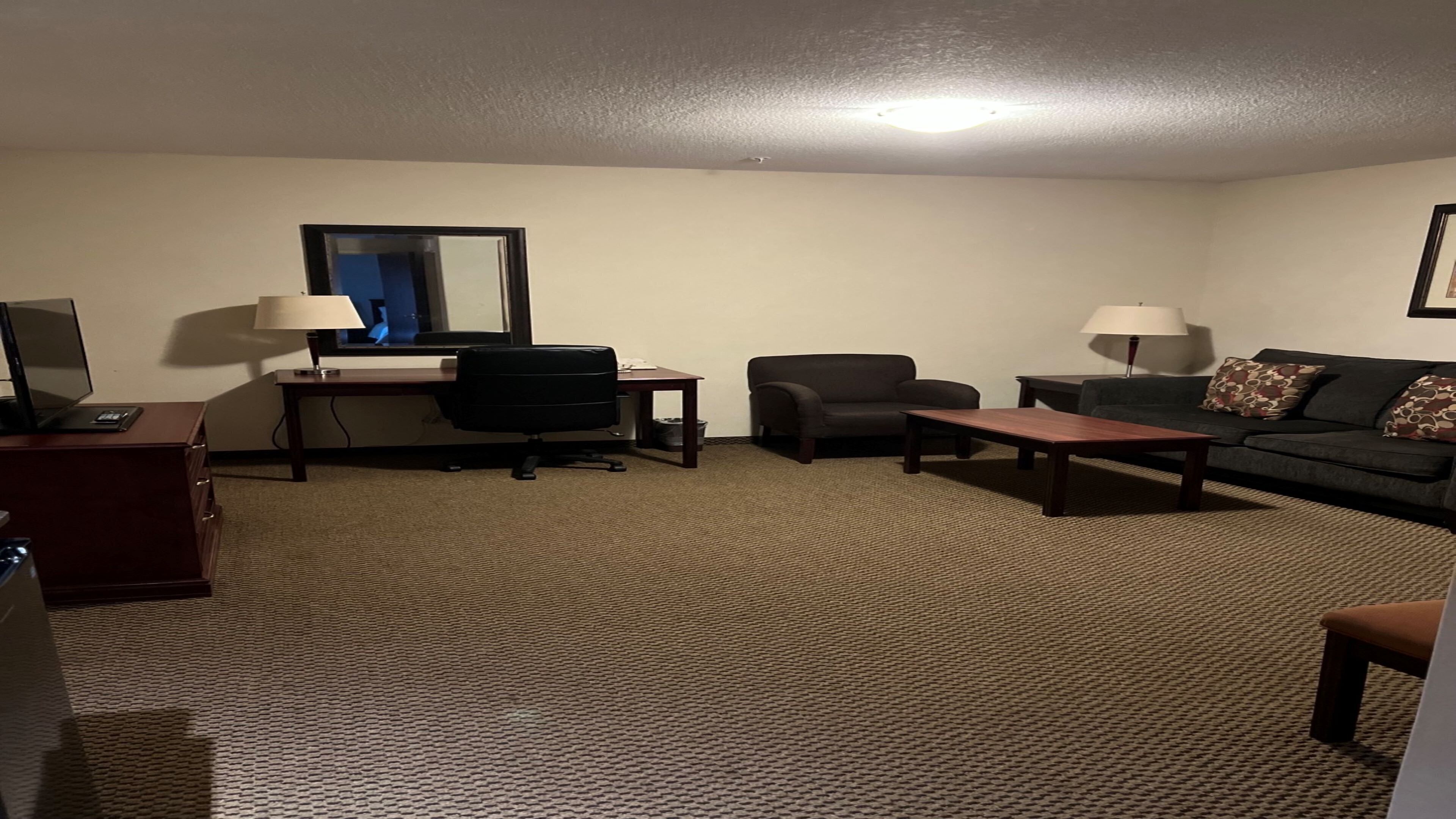 A hotel room with a desk, office chair, sofa, and a television.