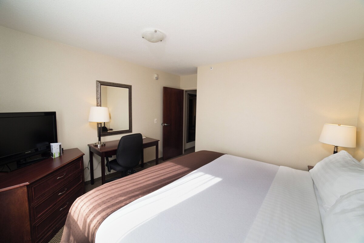 A hotel room with a bed, a desk, a television, a mirror, and a door.