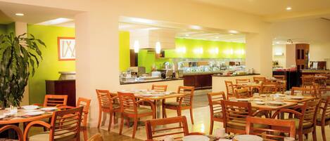 Un comedor con varias mesas y sillas, un mostrador de buffet y una planta grande en maceta.
