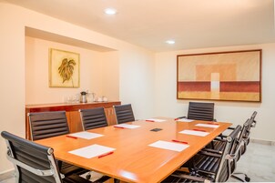 A conference room with a long table, black chairs, and a wooden cabinet with a coffee machine.